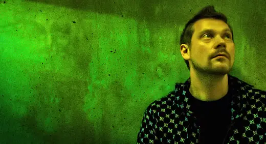 A man standing in front of a green wall, potentially engaged in beatmaking or music production online using a free program.