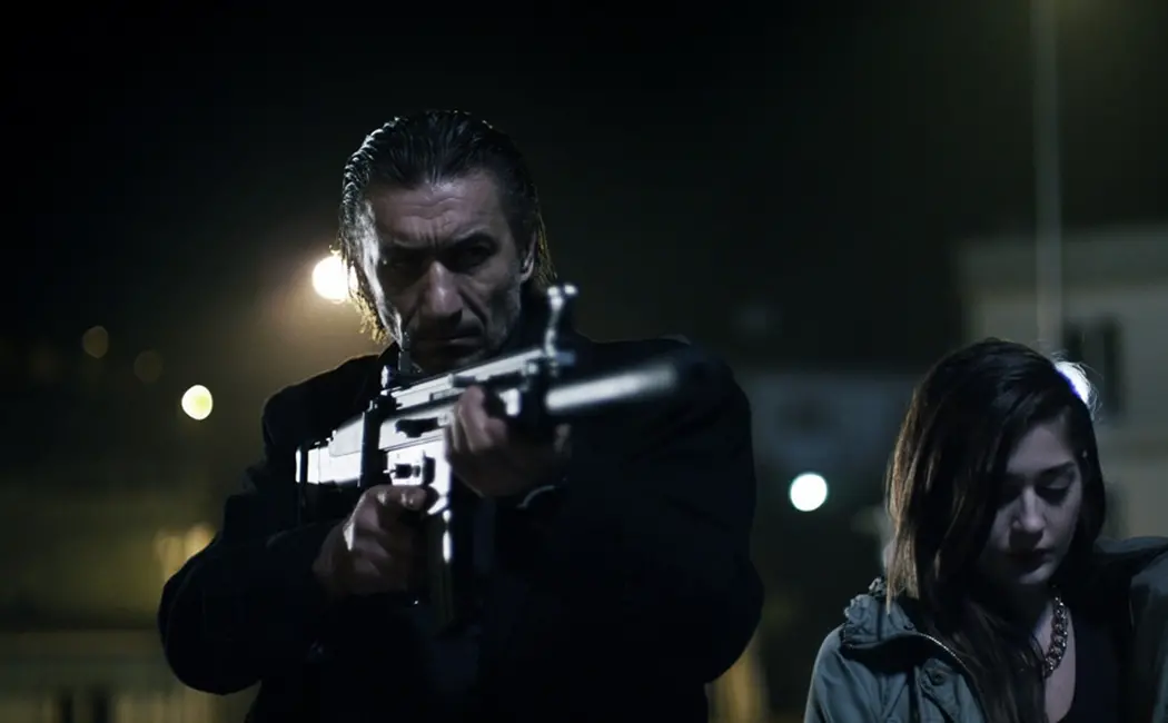 A man with a gun is standing next to a woman, creating an intense atmosphere.