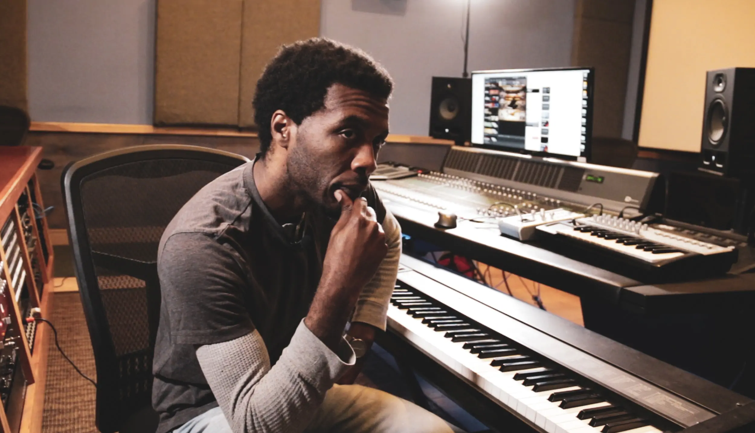 A music producer sitting in front of a keyboard in a recording studio, using a music production program.
