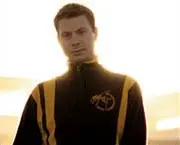 A man in a yellow and black jacket standing in front of a field while exploring music production programs.