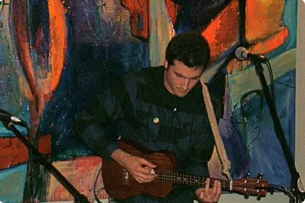 A man playing a guitar in front of a painting, showcasing his musical talent.