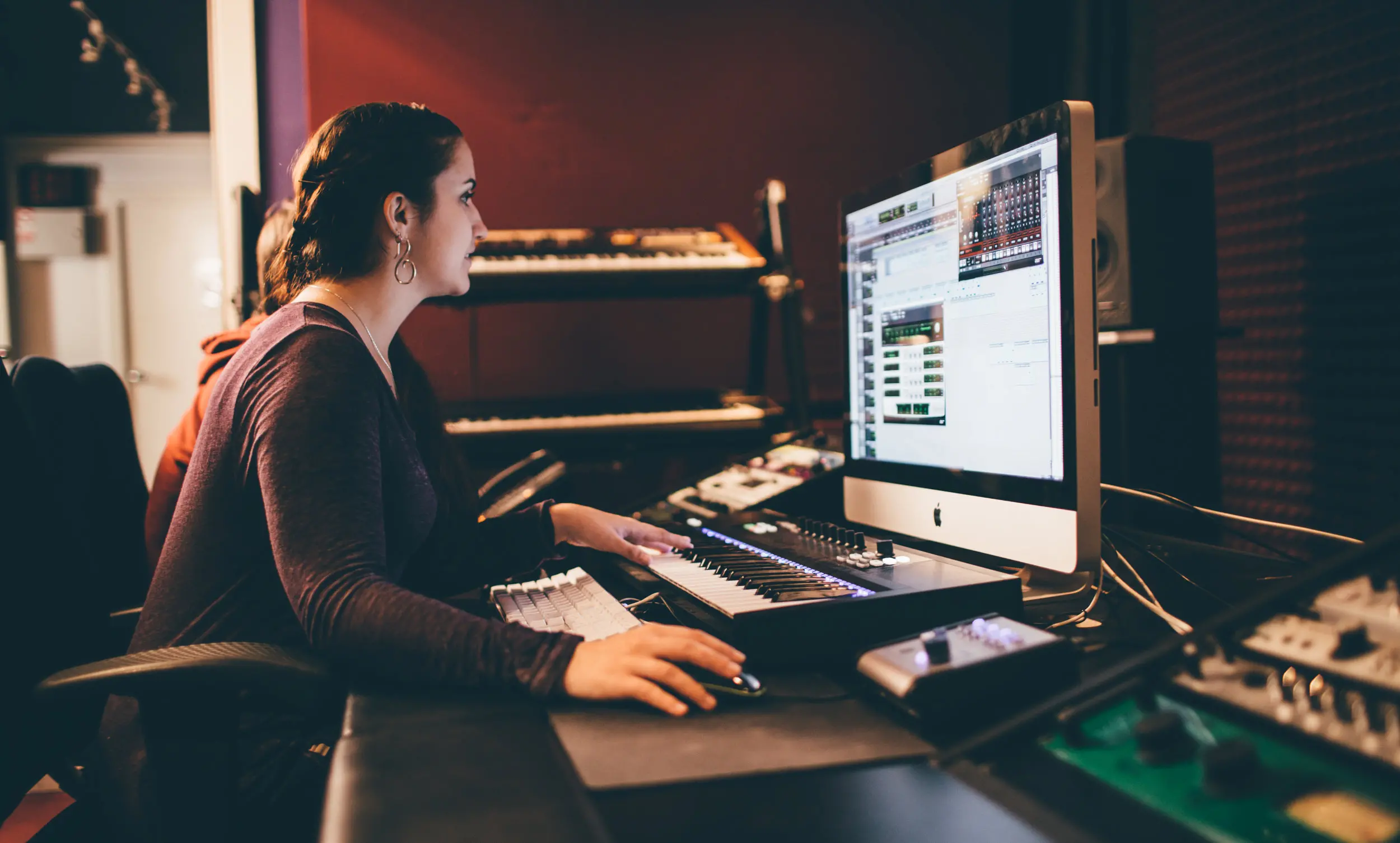 An experienced music producer engrossed in beatmaking on a computer in a recording studio.