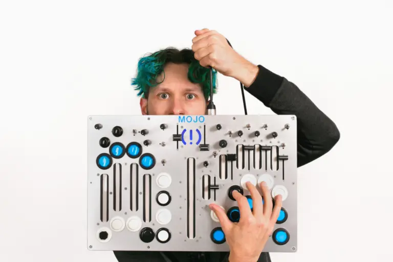 A music producer with blue hair holding up a large electronic board.