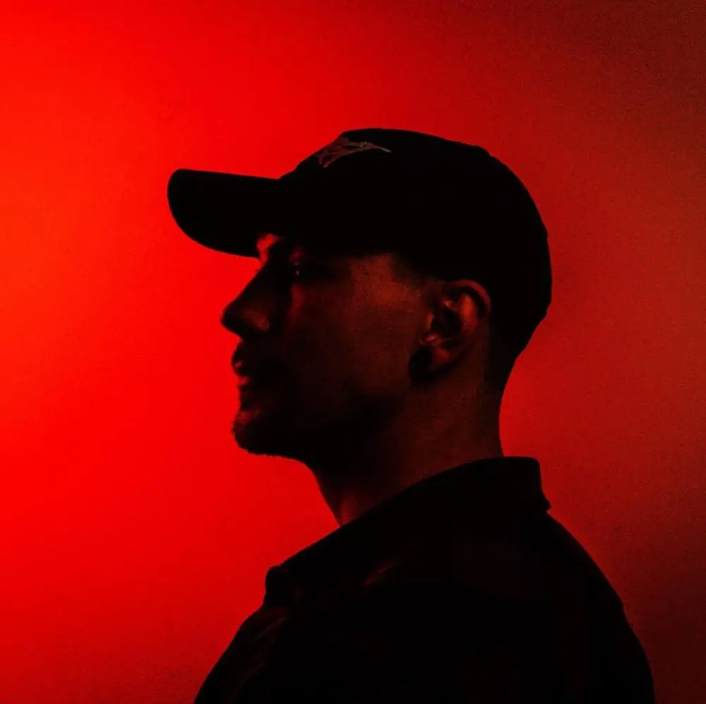 A silhouette of a man standing in front of a red light, creating music with a music production program.