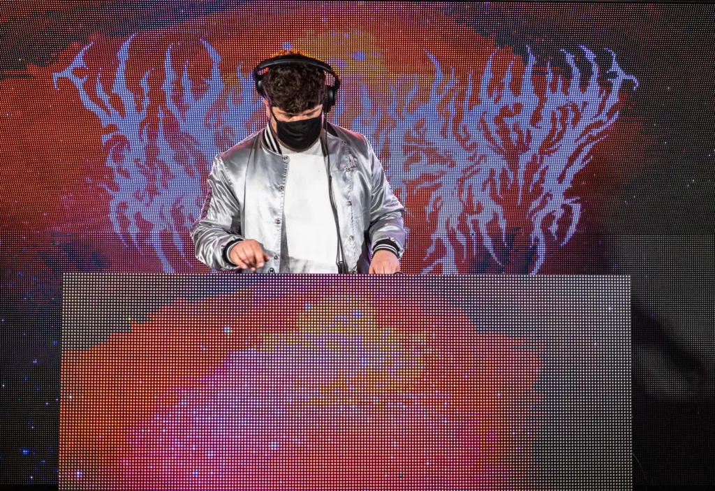 A man in a silver jacket is beatmaking and mixing tracks on a stage.