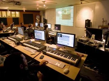 A group of people sitting at desks in a music production studio, utilizing a music production program.