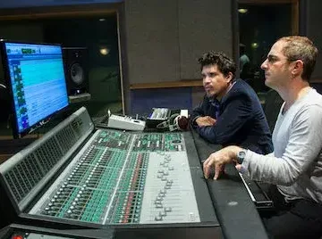 Two men passionately engaged in beatmaking at a recording studio, while expertly handling a mixing board for optimal mixing and mastering.