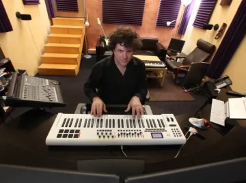 A music producer playing an electronic keyboard in a recording studio.