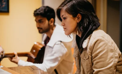 Two people sitting at a table listening to music and using a music production program.